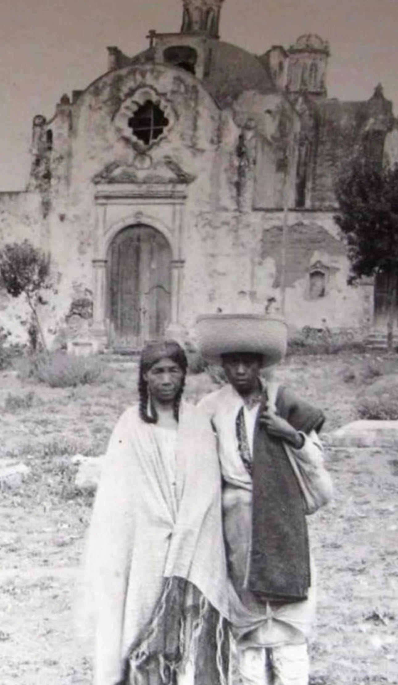 Two Indigenous people standing before a colonial-era church — historical photograph