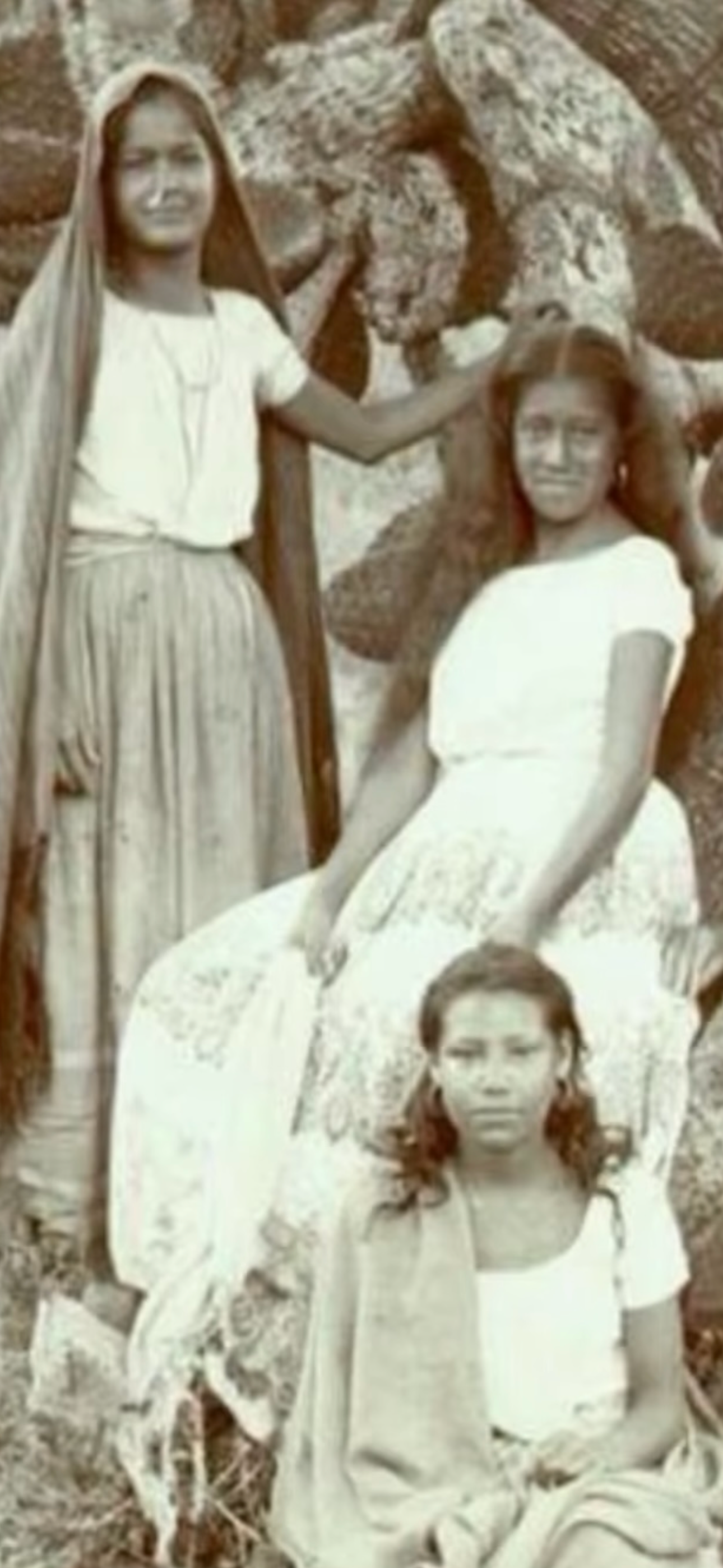 Three Indigenous women and girls in white dresses outdoors — historical photograph